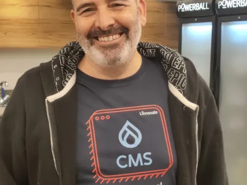 Smiling man in a CMS-themed t-shirt stands indoors with coolers in the background.