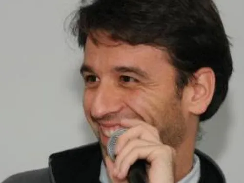 Man smiling while holding a microphone and speaking.