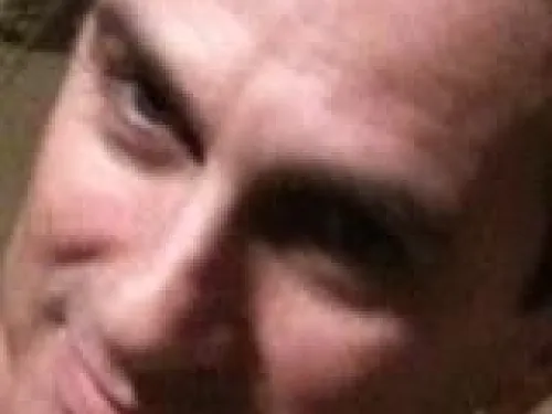 Man with short dark hair smiling slightly, close-up of face.
