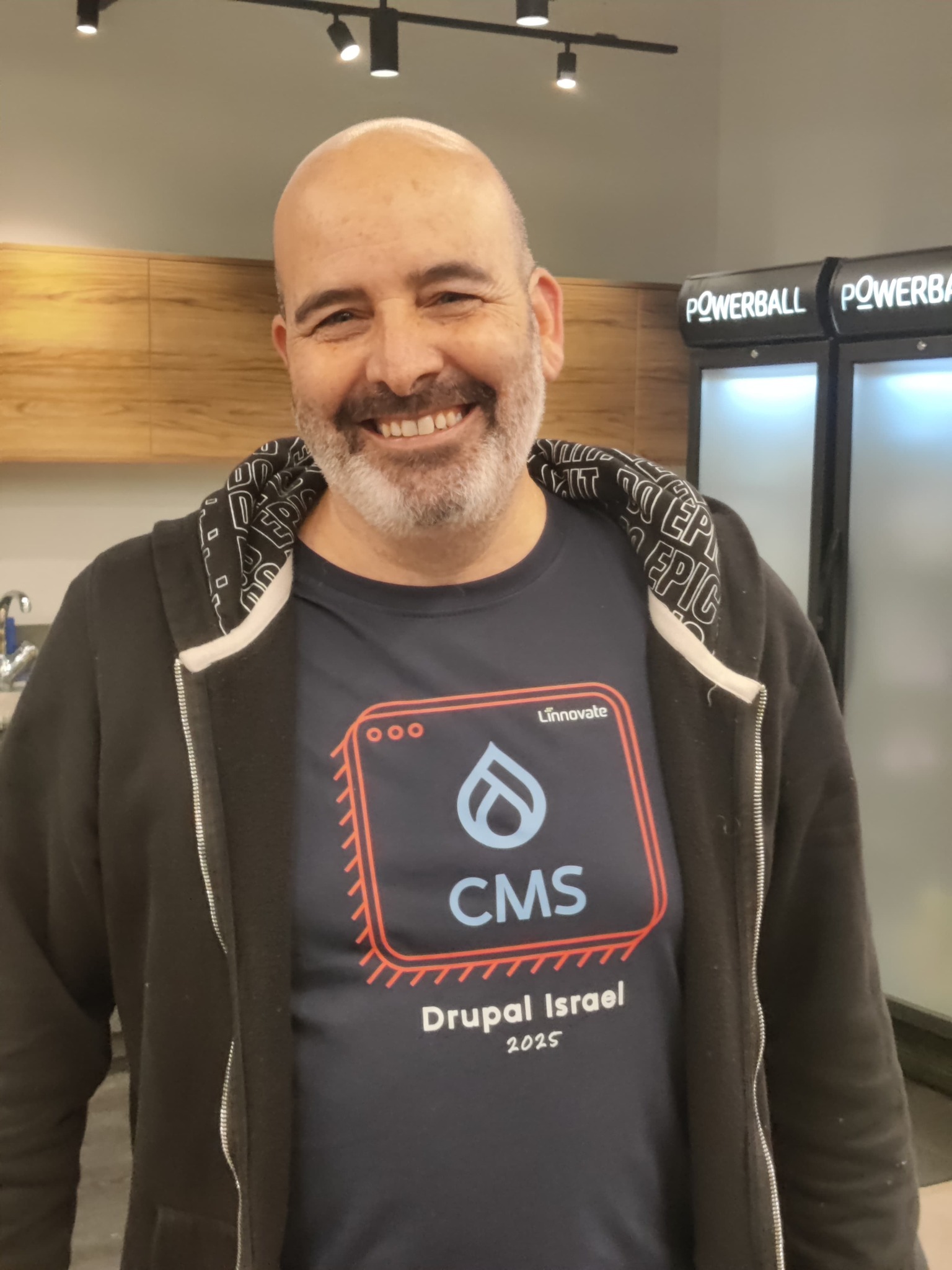 Smiling man in a CMS-themed t-shirt stands indoors with coolers in the background.
