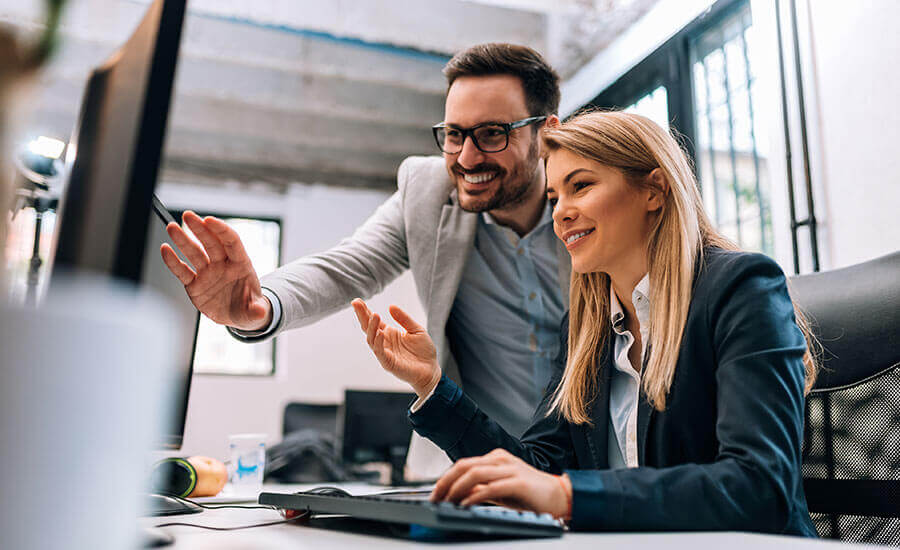 Two colleagues smiling and collaborating at a computer in a modern office.
