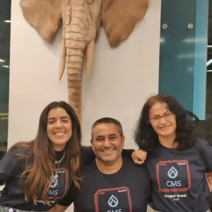 Three people smiling in front of an elephant wall sculpture.