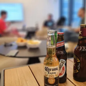 Three beer bottles on a table with people having a meeting in the background.