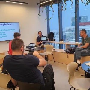 Four people in a modern meeting room with snacks and a presentation screen.