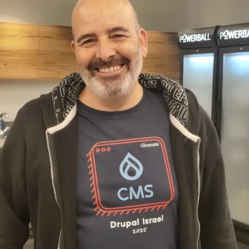 Smiling man in a CMS-themed t-shirt stands indoors with coolers in the background.