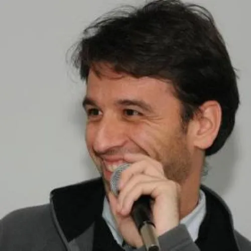 Man smiling while holding a microphone and speaking.