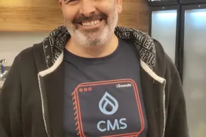 Smiling man in a CMS-themed t-shirt stands indoors with coolers in the background.