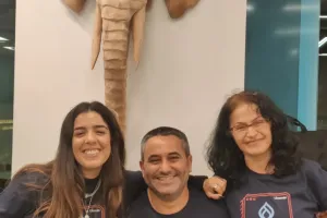 Three people smiling in front of an elephant wall sculpture.