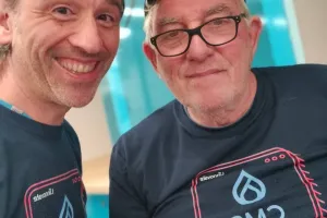 Two smiling men wearing matching navy CMS t-shirts, one with glasses and a cap.