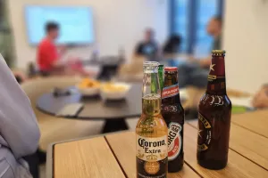 Three beer bottles on a table with people having a meeting in the background.