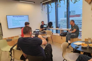 Four people in a modern meeting room with snacks and a presentation screen.