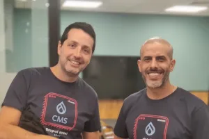 Two drupal developers smiling and standing in an office, both wearing matching navy blue t-shirts.