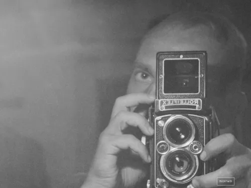Person holding a vintage camera, reflected in a mirror, with Hebrew text overlay.